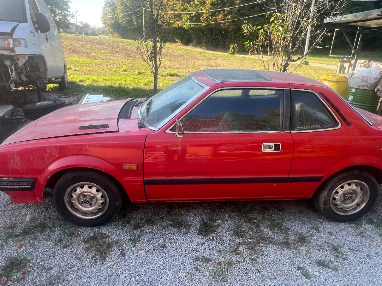 The red Honda Prelude seen from the left side in the yard.